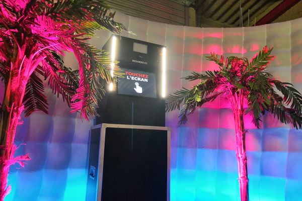 un photobooth installé avec des décorations autour (palmiers et spot de couleur bleu et rose).
