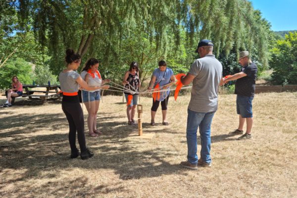 six personnes qui tiennent une ficelle avec un grappin et portent un brassard orange. Sur une plaine sous un arbre