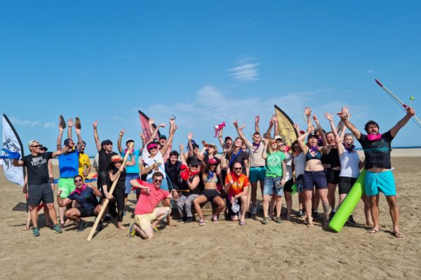 un groupe de personnes qui lèvent les bras sur la plage. Avec des objets d'aventuriers dans les mains et des drapeaux en arrière plan