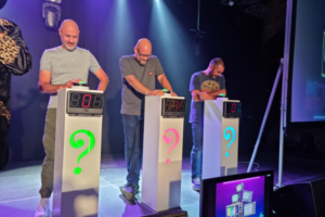 Trois personnes qui réfléchissent derrière un pupitre et un buzzer.