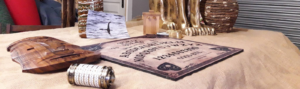 une table de ouija, un casse-tête, un totem et un chat doré sont posés sur une table avec une toile de jute